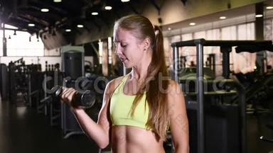 体育运动的女人手里拿着哑铃。 活泼活泼的年轻女子对着镜头微笑。 健身房背景。 健康健康